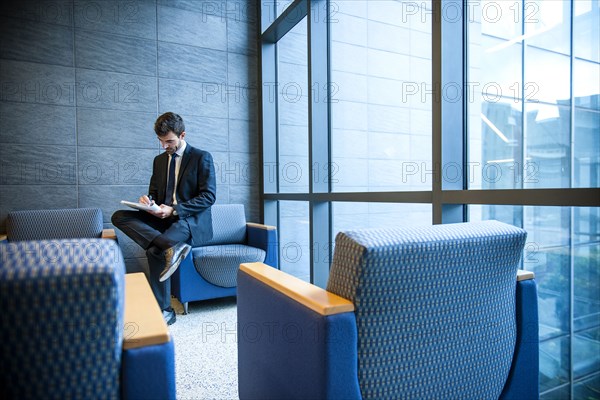 Hispanic businessman writing on notepad in office lounge