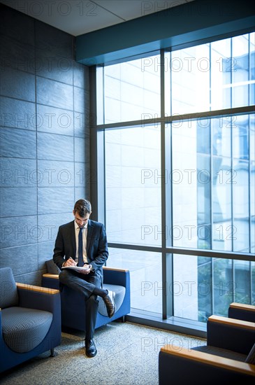 Hispanic businessman writing on notepad in office lounge