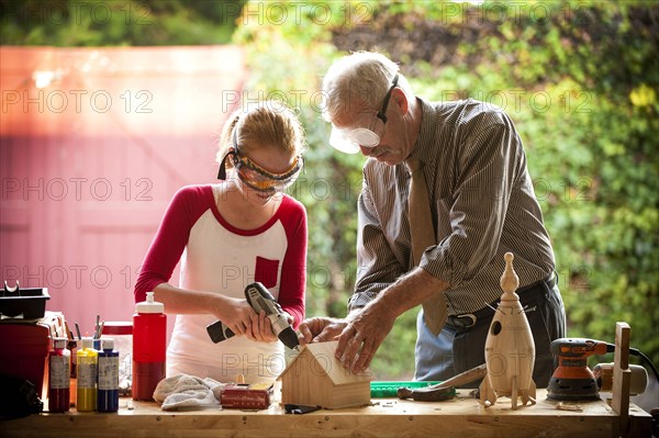 Grandfather helping granddaughter build birdhouse in garage