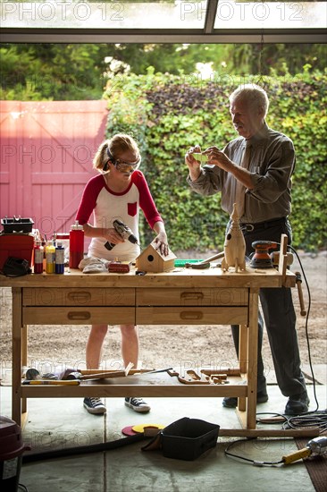 Grandfather photographing granddaughter building birdhouse in garage