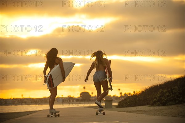 Teenage girls carrying surfboards on skateboards