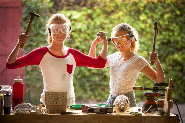 Sisters flexing muscles and holding hammers