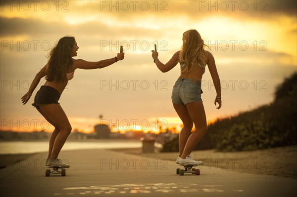 Teenage girls riding skateboards holding cell phones