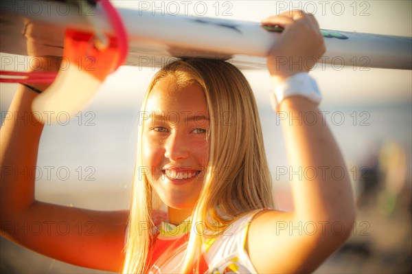 Smiling Caucasian teenage girl balancing surfboard on top of head