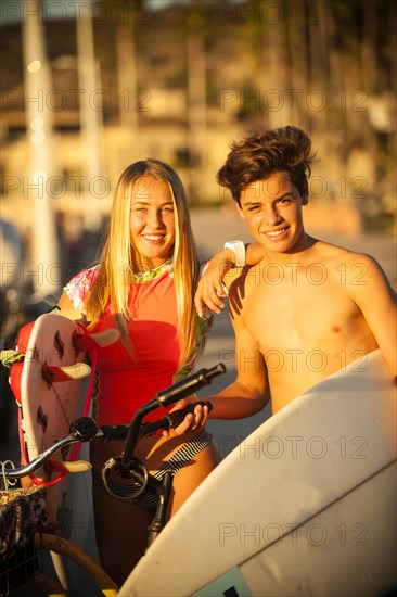 Teenage boy and girl posing with surfboards and bicycles