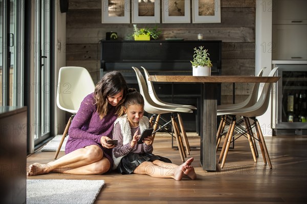 Smiling mother and daughter sitting on floor texting on cell phones