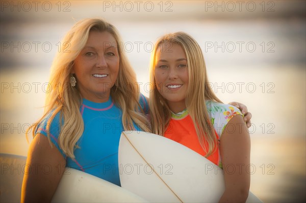 Portrait of smiling Caucasian mother and daughter holding surfboards