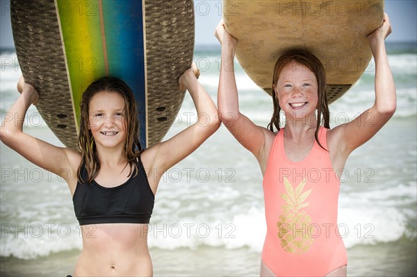 Portrait of smiling girls balancing surfboards on top of heads