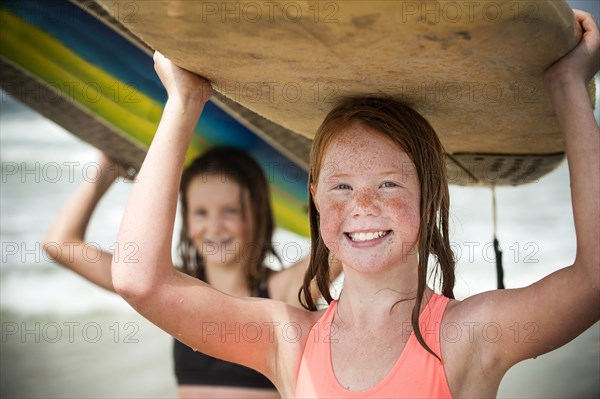 Portrait of smiling girls balancing surfboards on top of heads