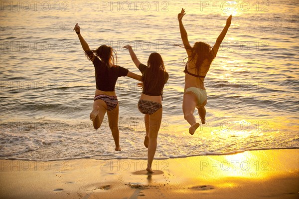 Teenage girls running into ocean at sunset