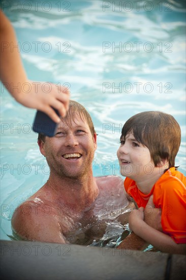 Hand holding cell phone for Caucasian father and son in swimming pool