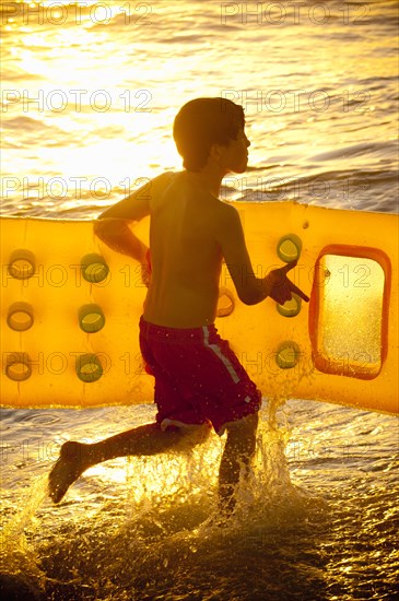 Caucasian boy running into ocean carrying inflatable raft