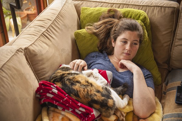 Caucasian girl laying on sofa petting cat