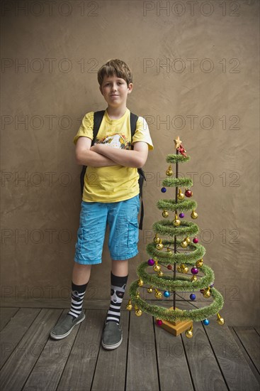 Portrait of Caucasian boy standing near small artificial Christmas tree
