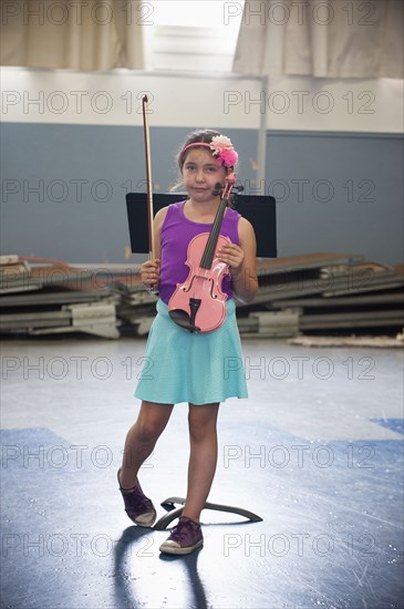 Portrait of awkward Hispanic girl holding pink violin