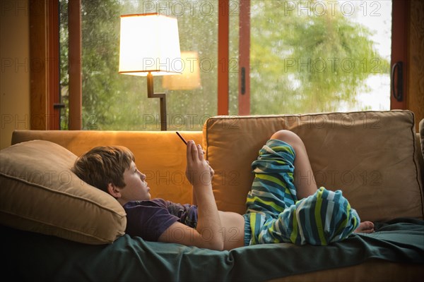 Caucasian boy laying on sofa texting on cell phone