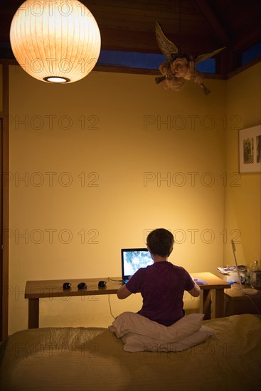 Caucasian boy sitting on bed using laptop