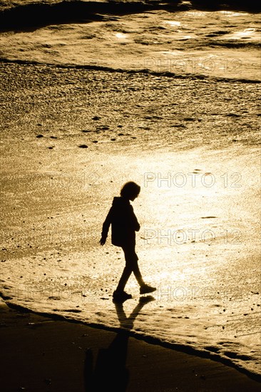 Silhouette of mixed race boy walking on beach at sunset