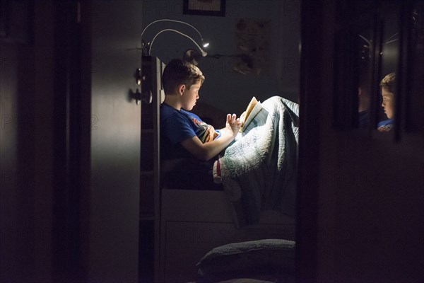 Caucasian boy reading book in bed at night