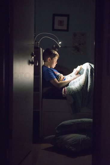 Caucasian boy reading book in bed at night