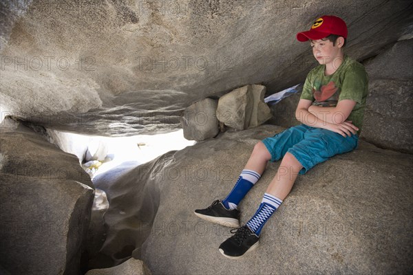 Pensive Caucasian boy sitting on rocks