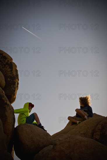 Boys sitting on rocks under blue sky