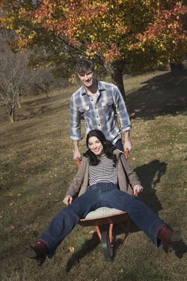 Caucasian man pushing wife in wheelbarrow