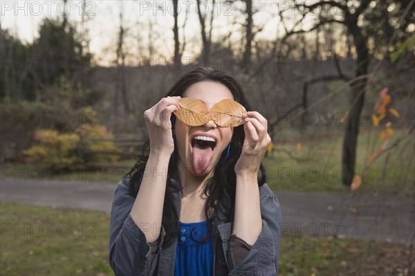 Playful Caucasian woman with leaves covering her eyes