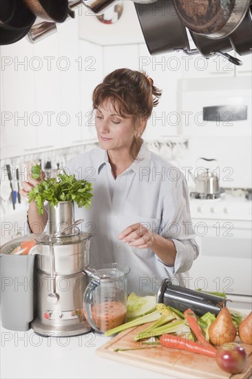 Caucasian woman juicing vegetables in kitchen