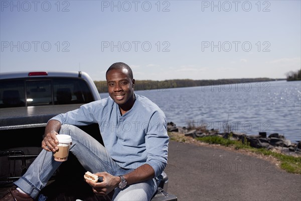 Black man sitting in truck bed eating lunch