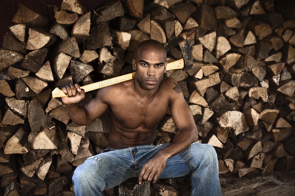 Bare chested African American man near woodpile holding ax