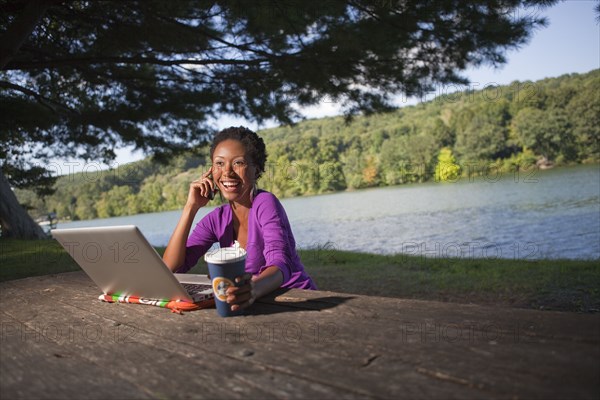 African American businesswoman sitting at picnic bench talking on cell phone