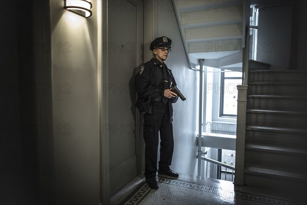 Older Caucasian policewoman holding gun in apartment staircase