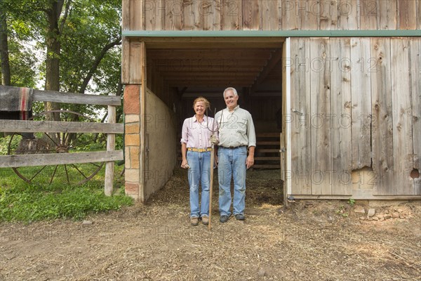 Older Caucasian couple standing by barn on farm