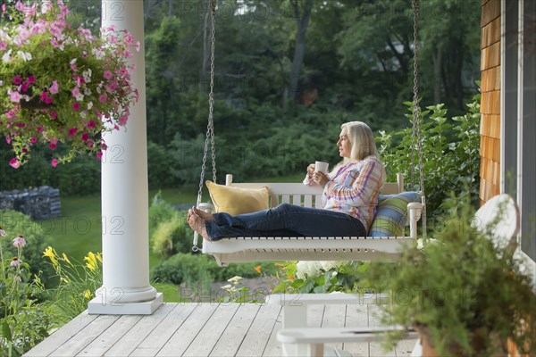 Older Caucasian woman drinking cup of coffee on porch swing
