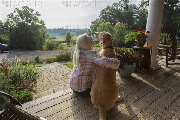 Older Caucasian woman petting dog on front porch