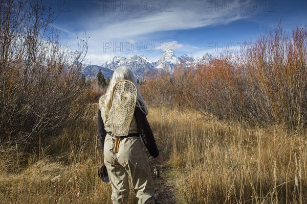 Older Caucasian woman carrying fishing supplies in field