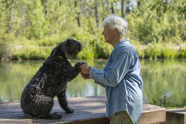 Older Caucasian woman shaking paw of dog in park