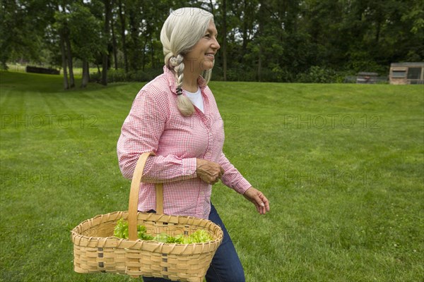 Caucasian woman carrying basket of vegetables in garden