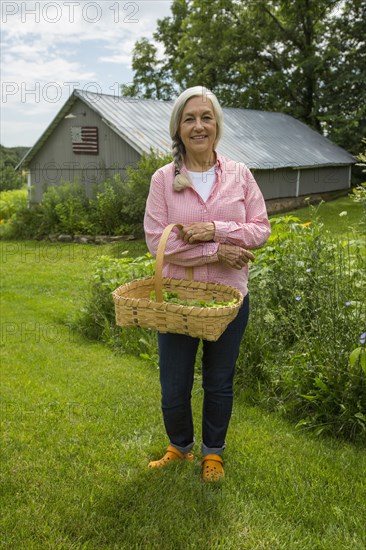 Caucasian woman carrying basket of vegetables in garden