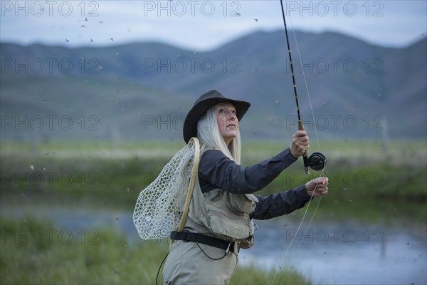 Caucasian woman casting fishing line in remote lake