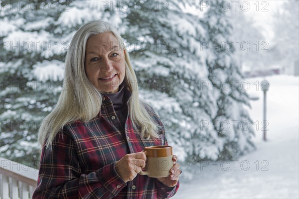 Older Caucasian woman drinking coffee on snowy patio