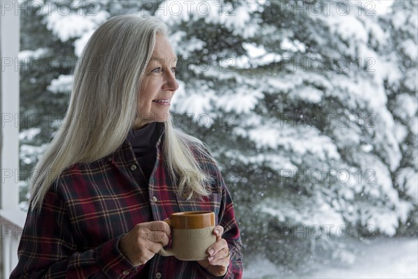 Older Caucasian woman drinking coffee on snowy patio