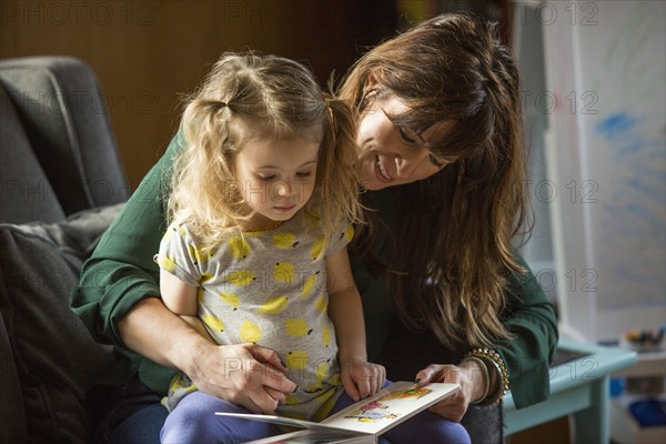 Caucasian mother and daughter reading book on sofa