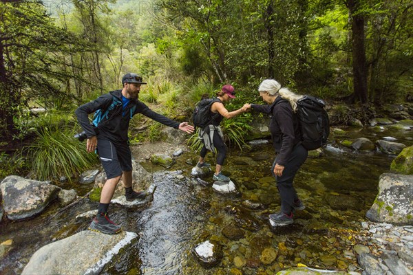 Caucasian hikers crossing creek on rocks in forest