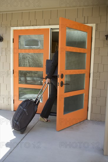 Businesswoman pulling rolling suitcase through doorway