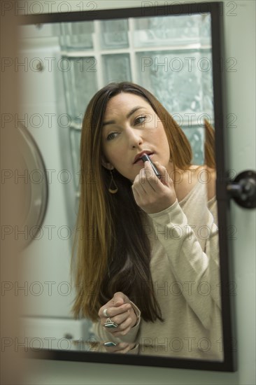 Woman applying lipstick in mirror