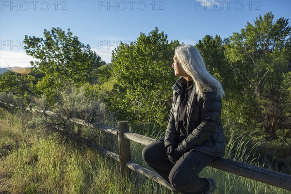 Older Caucasian woman sitting on wooden fence