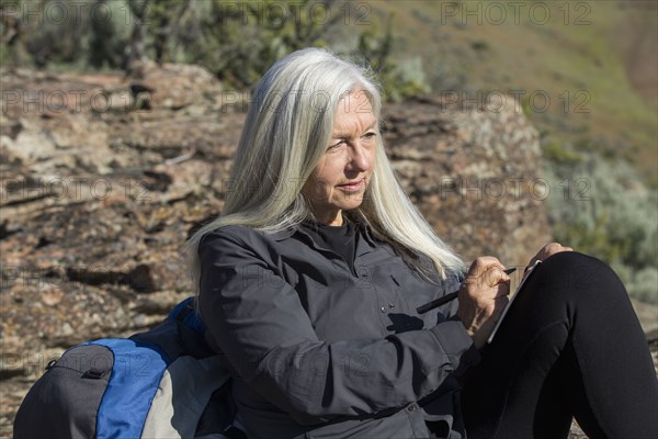 Older Caucasian woman leaning on rock writing in journal