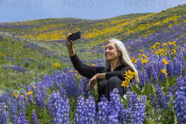 Caucasian woman posing for cell phone selfie hillside with wildflowers